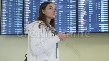可爱的女孩使用智能手机站在董事会的背景上，并安排在机场的起飞时间