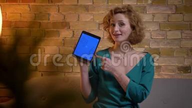 <strong>姜黄色</strong>卷发的白种人女孩的特写肖像，在舒适的家中愉快地展示了蓝色的平板电脑屏幕