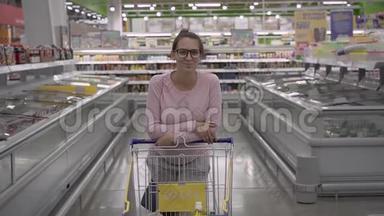 一个带眼镜的年轻孕妇站在<strong>超市</strong>里，靠在手推车上。 做<strong>杂货</strong>店购物的女人。