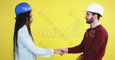 在一个黄色背景墙的工作室里，两<strong>位</strong>建筑师，一<strong>位</strong>非洲女士和一<strong>位</strong>戴着蓝白头盔的男人