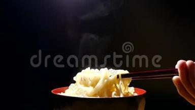 筷子到美味的面条，蒸汽和烟雾在碗的黑色背景下缓慢运动，亚洲餐特写，垃圾食品和FA。