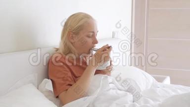 一个女人，一张悲<strong>伤痛</strong>苦的脸，坐在白色毯子下的床上，吃着一盘汤。