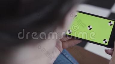 黑头发的女少女使用绿色屏幕的智能手机，坐在室内。 库存录像。 女人拿着手机
