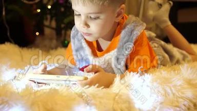孩子躺在孩子们房间里柔软`白色毯子上。 他正在智能手机上看动画片。 圣诞节
