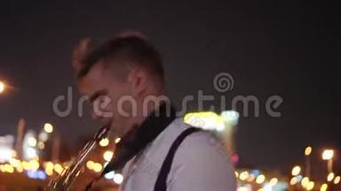 街头音乐家在夜晚城市的背景下在海滨演奏萨克斯风。 很漂亮的夜灯。