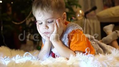 孩子躺在孩子们房间里柔软`白色毯子上。 他正在智能手机上看动画片。 圣诞节