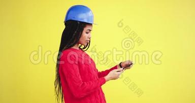 严肃的年轻女工程师在一个有黄色<strong>背景墙</strong>的工作室里用她的想象手机拍照