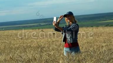 一个苗条的女人走在麦田上，在阳光明媚的夏<strong>日</strong>在<strong>手机</strong>上拍照小穗。