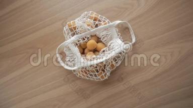 手放在网状有机串袋上，水果放在木桌上。 经合组织，零废物