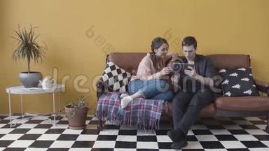 一对夫妇坐在沙发上，带着电子平板电脑，在一<strong>黄</strong>色的墙壁和<strong>黑白</strong>格子地板