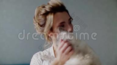 美丽的女孩穿着白色睡衣，抱着一只暹罗猫，抚摸着他的手。 他抚摸他的脖子
