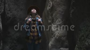 洞穴或峡谷中的女旅行者。 她戴着一顶帽子和一件夹克，有一个背包。 探索一个古老的洞穴