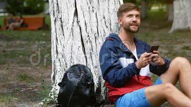 坐在树下的小胡子男人用手机打字。 学生在公园里聊天