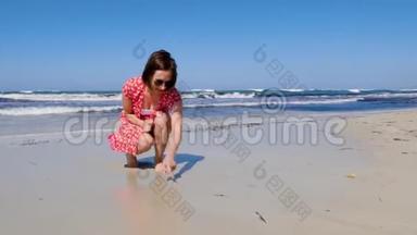 年轻迷人的<strong>女人</strong>在一个孤独的沙滩上画着心脏标志，强烈的波浪撞击着海岸。 她穿着红裙子，<strong>晒太阳</strong>