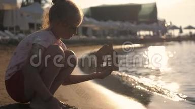 日落时，女孩在海滩上拿着纸房子。 人，梦想，家庭，房地产和家居理念.. 儿童梦