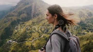 特写镜头，年轻的旅游妇女带着背包和相机在她的头发上享受风在惊人的山景。