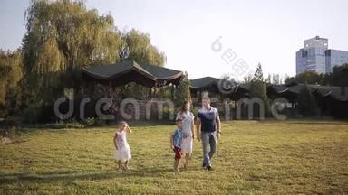 妈妈，爸爸，儿子和女儿周末牵着手在公园里散步。 幸福的家庭。