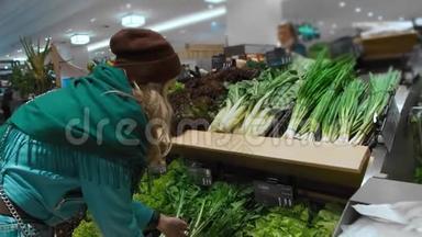 美丽的白种人女孩穿着蓝色夹克和绿色围巾，选择并购买绿色蔬菜和健康产品。