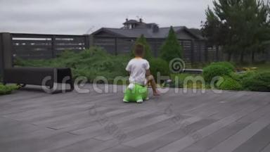 在绿色的花园里骑着绿色的玩具马的小男孩儿子跳跃-家庭价值观温暖的颜色夏天的场景