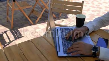 一个穿着白色衬衫的男人坐在街头咖啡馆的桌子旁，在<strong>笔记本</strong>电脑键盘上打字。 从<strong>上面</strong>看。 4k. 4k视频
