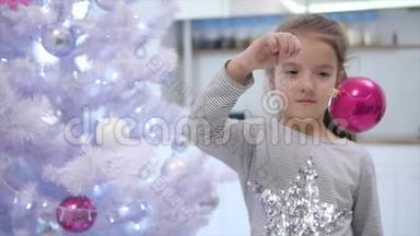 可爱的孩子玩一个粉红色的宝布尔，左右摇摆，站在圣诞树附近，微笑。