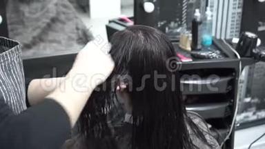 女孩坐在<strong>镜子</strong>前的<strong>理发店</strong>里，理发师用梳子梳湿了的头发