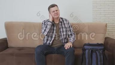 一个中年男人坐在<strong>沙发</strong>上，耳朵疼。 <strong>沙发</strong>旁边是一个<strong>大</strong>型旅游背包。