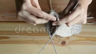 年轻妇女在木桌背景上用灰色金属针和羊毛线编织
