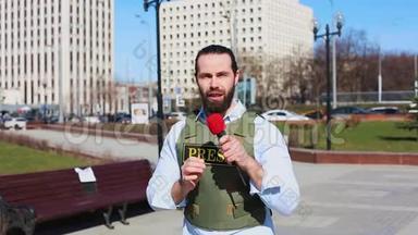 中弹，男电视记者穿着防弹衣在摩天大楼前对着麦克风说话