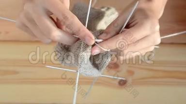 年轻妇女在木桌背景上用灰色金属针和羊毛线编织