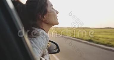 美丽的女孩把手伸出车窗外，在阳光明媚的天气里微笑。 慢动作