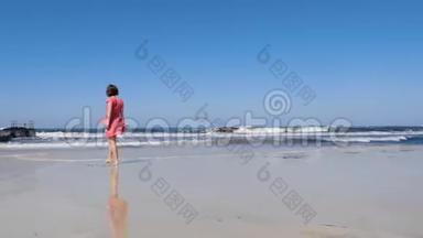 年轻迷人的女人走向海滩上的相机，享受阳光和风。 海上码头蓝天和暴风雨波浪