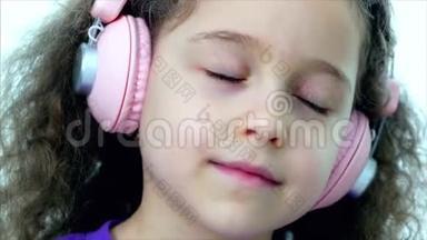 一个卷发可爱的孩子的肖像，一个穿着<strong>紫</strong>色t恤，戴着<strong>粉色</strong>耳机听着的白种人小女孩