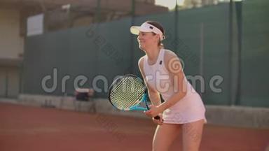 快乐的运动员等待网球。 熟练的女网球运动员正准备打一个球。 她手里拿着