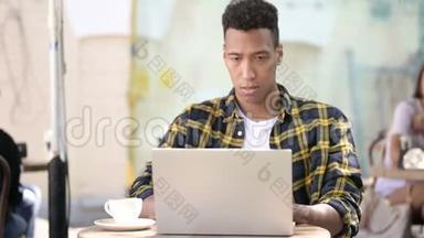 非洲青年男子对笔记本电脑、户外咖啡厅的成绩感到沮丧