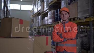 工人的肖像，双手交叉在胸前，站在明亮的橙色制服附近，仓库里的许多箱子