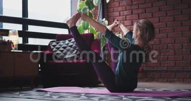 金发女郎伸展双腿，在客厅的家里练习瑜伽，她身材健美，穿着舒适的衣服