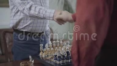 两个人在开始比<strong>赛前</strong>在棋盘上握手，坐在小桌旁。 美丽的国际象棋