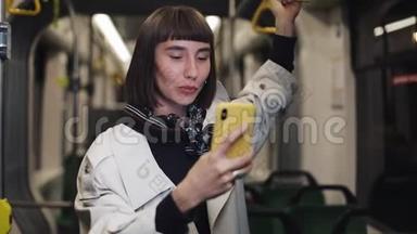 年轻的微笑女子在乘坐公共交通工具时有一个视频电话。 城市灯光背景。