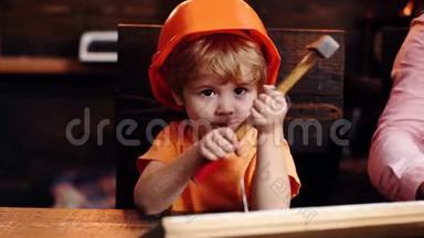 戴着头盔的孩子，可爱地扮演建筑工人或修理工，修理或手工制作。 小孩把钉子钉在木板上