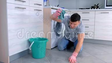 快乐的男人戴着橡胶手套，在厨房里<strong>使劲</strong>地擦地板，坐在地板上，侧视。