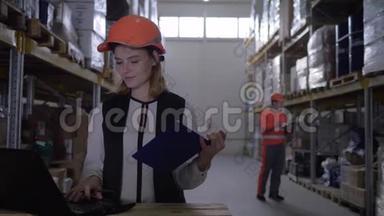 戴安全帽的<strong>员工</strong>女士<strong>使用</strong>笔记本电脑，并在仓库工人的背景下在记事本上做笔记