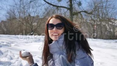 早上，穿着黑色太阳镜和黑色<strong>直发</strong>的年轻女孩在公园户外玩雪球