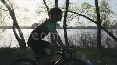 带胡子的年轻骑自行车的人穿着黑色的衣服喝水。 在沿河公园骑自行车轻松恢复。 慢动作