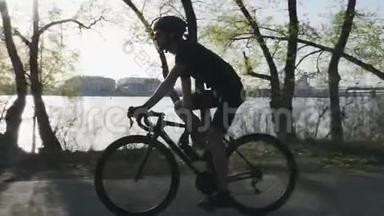 瘦小的三项运动员在自行车饮水。 阳光透过树木照耀。 训练期间口渴的三项运动员喝水.. 三项<strong>全能</strong>