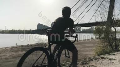 强壮健康的运动骑自行车的人坐在自行车上前方。 梦想着未来。 桥和河的背景。 慢慢