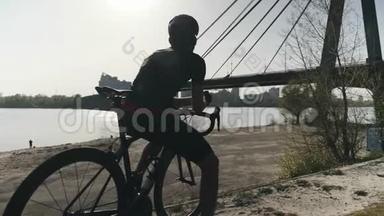 强壮健康的运动自行车手坐在自行车上看着前方。 梦想着未来。 桥和河的背景。
