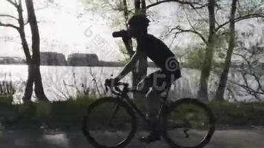 骑自行车时，骑自行车的人从水瓶里喝水。 口渴的骑自行车的人骑在城市公园沿河。