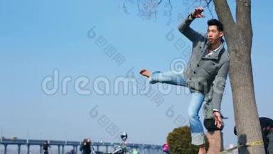 这个亚洲男人学会了在城市公园的树间伸展的绳子上平衡和行走。 男人平衡和跳跃