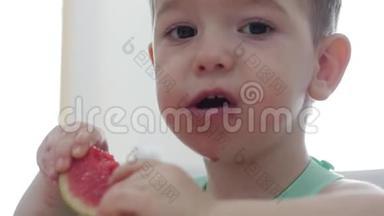 小孩子坐在围兜里的一张桌子旁吃自己的西瓜，可爱的宝宝心甘情愿地吃。 可爱的小宝宝